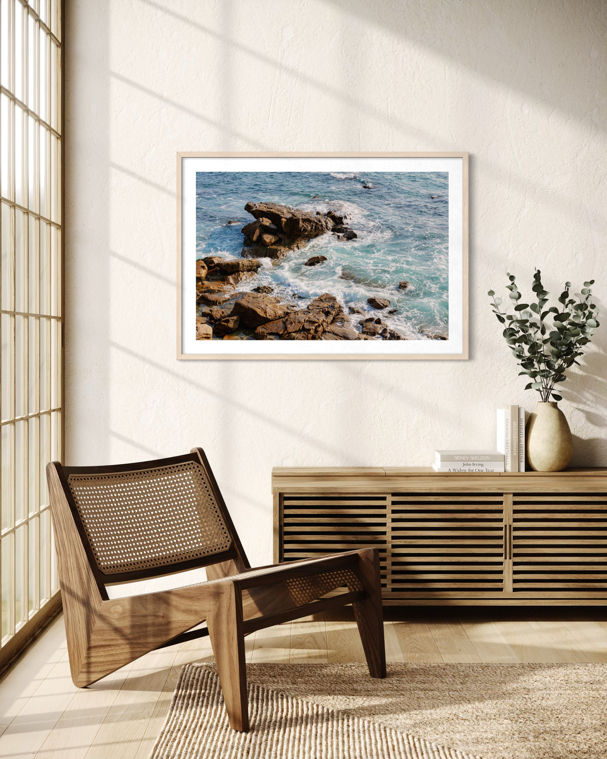 Laguna Beach ocean foam photograph on wall, with books, a vase, and wood furniture in a sunlit room.