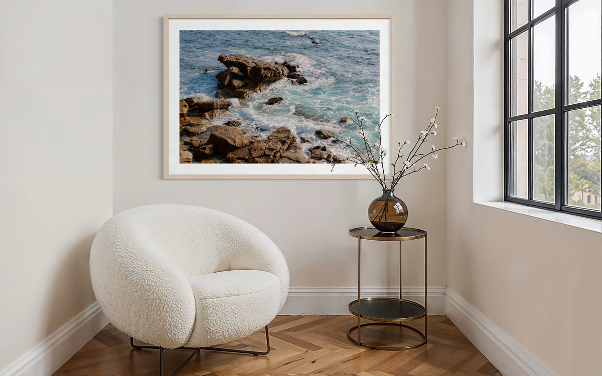 White chair and side table beside a window, “Ocean Foam” artwork displayed on the wall above.