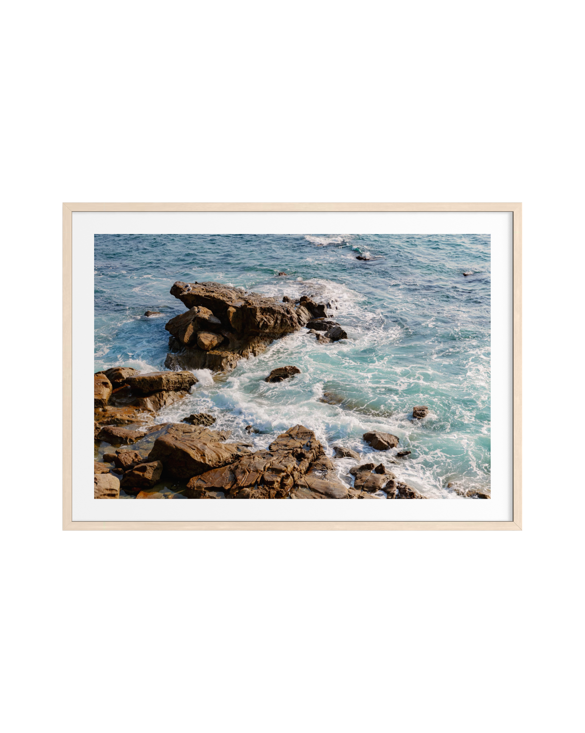 Turquoise waves with white foam crash against the rocky Laguna Beach shore under bright daylight.