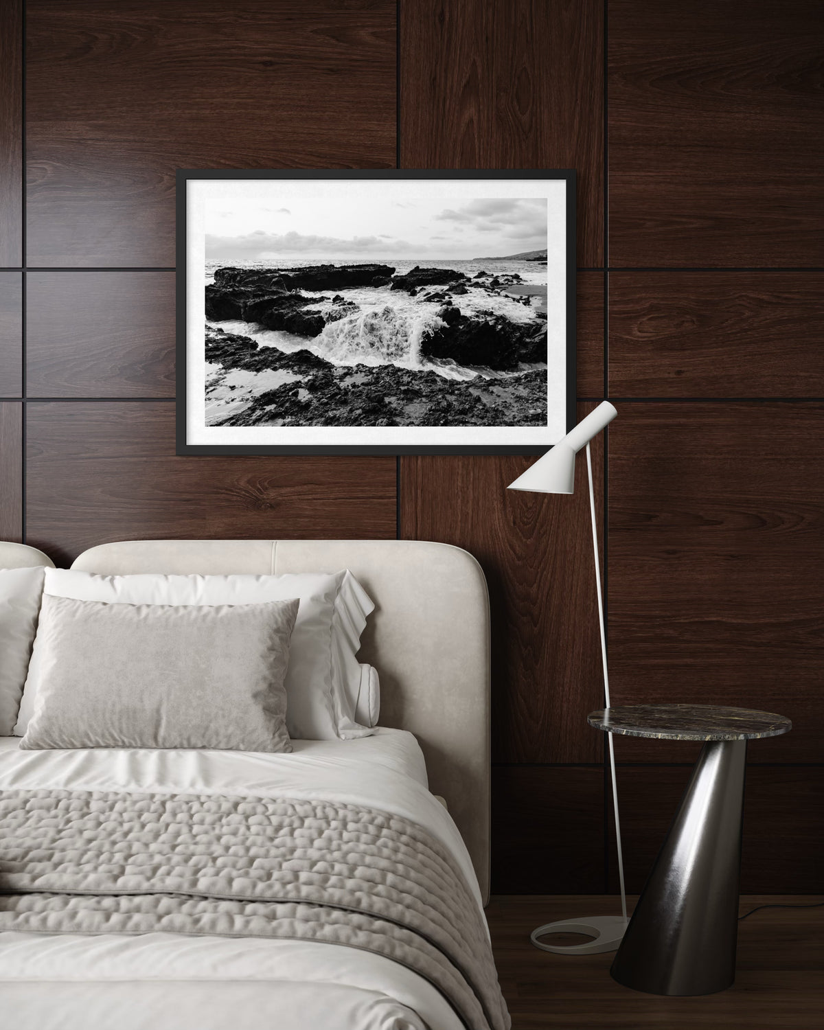 Framed Ocean Momentum wave print on a dark wood wall above a bed, next to a table and lamp.