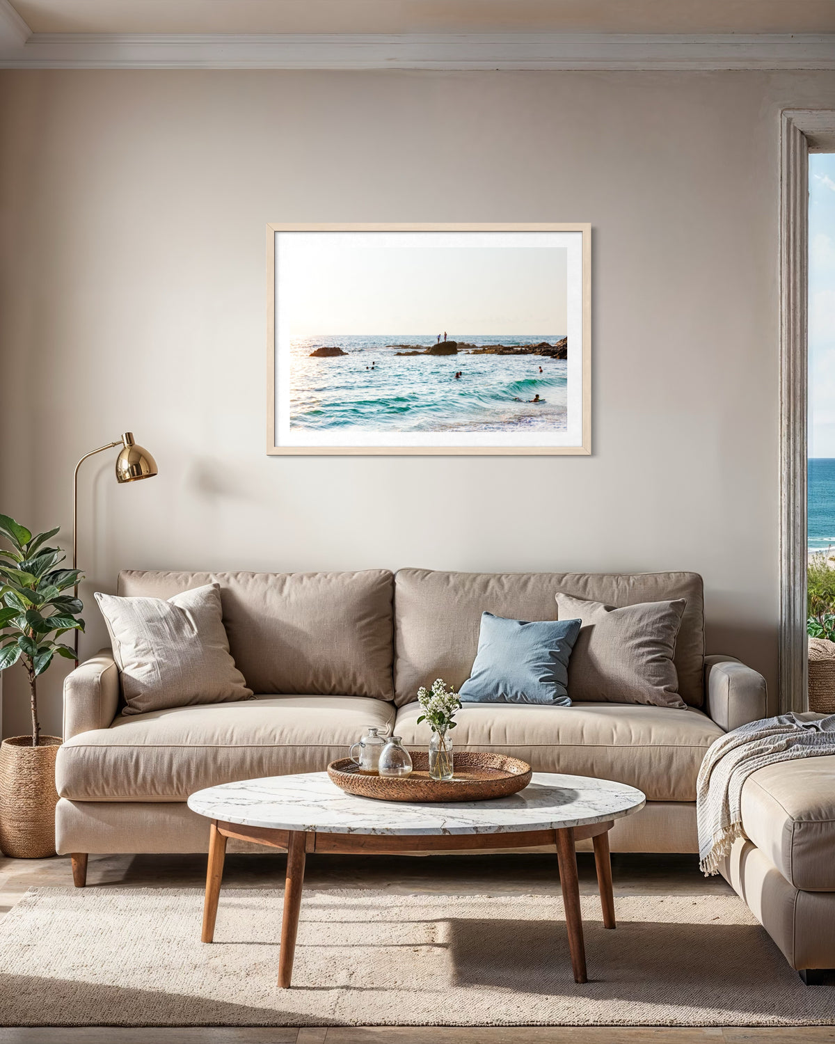 Beige sofa, blue pillows, and marble table in a bright living room with Ocean Swim artwork on the wall.