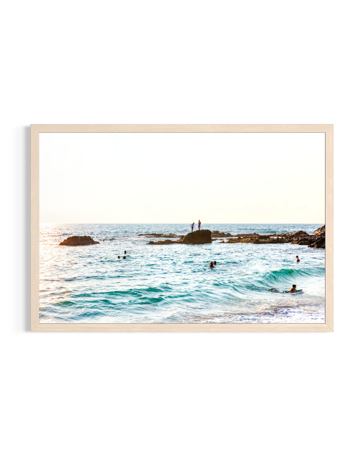Swimmers and surfers in Pacific waves with two people on rocks under the sun at Laguna Beach, California.