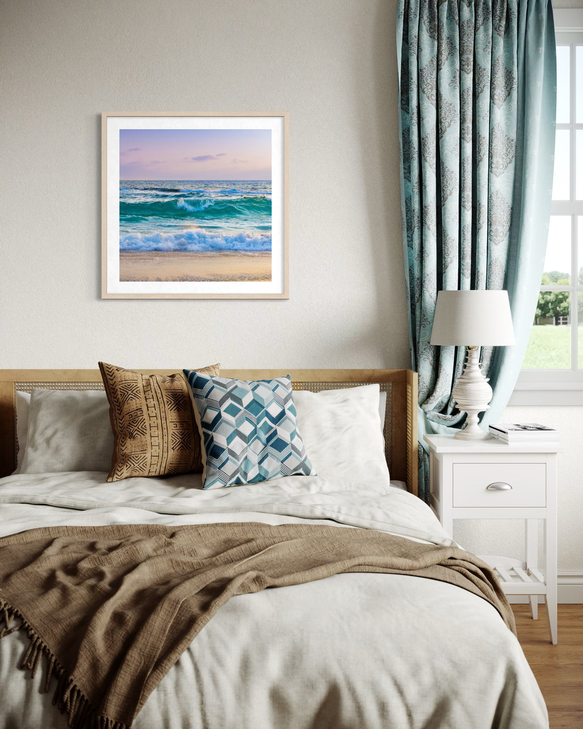 Bedroom with patterned pillows, a blanket, blue curtains, and “Ocean Waves II” artwork hanging above the bed.