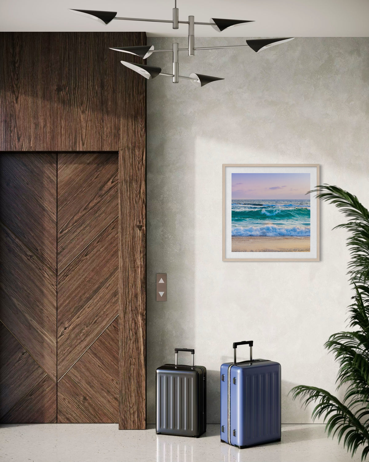 Two suitcases by a wooden elevator in a modern lobby with Ocean Waves II art and a potted plant.