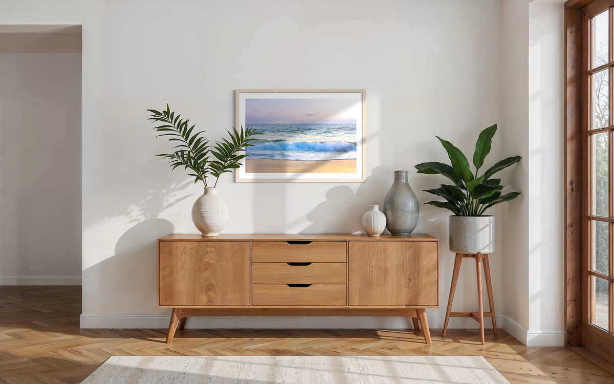 Framed “Ocean Waves” photo displayed above a wooden sideboard with plants and vases in a modern living room.