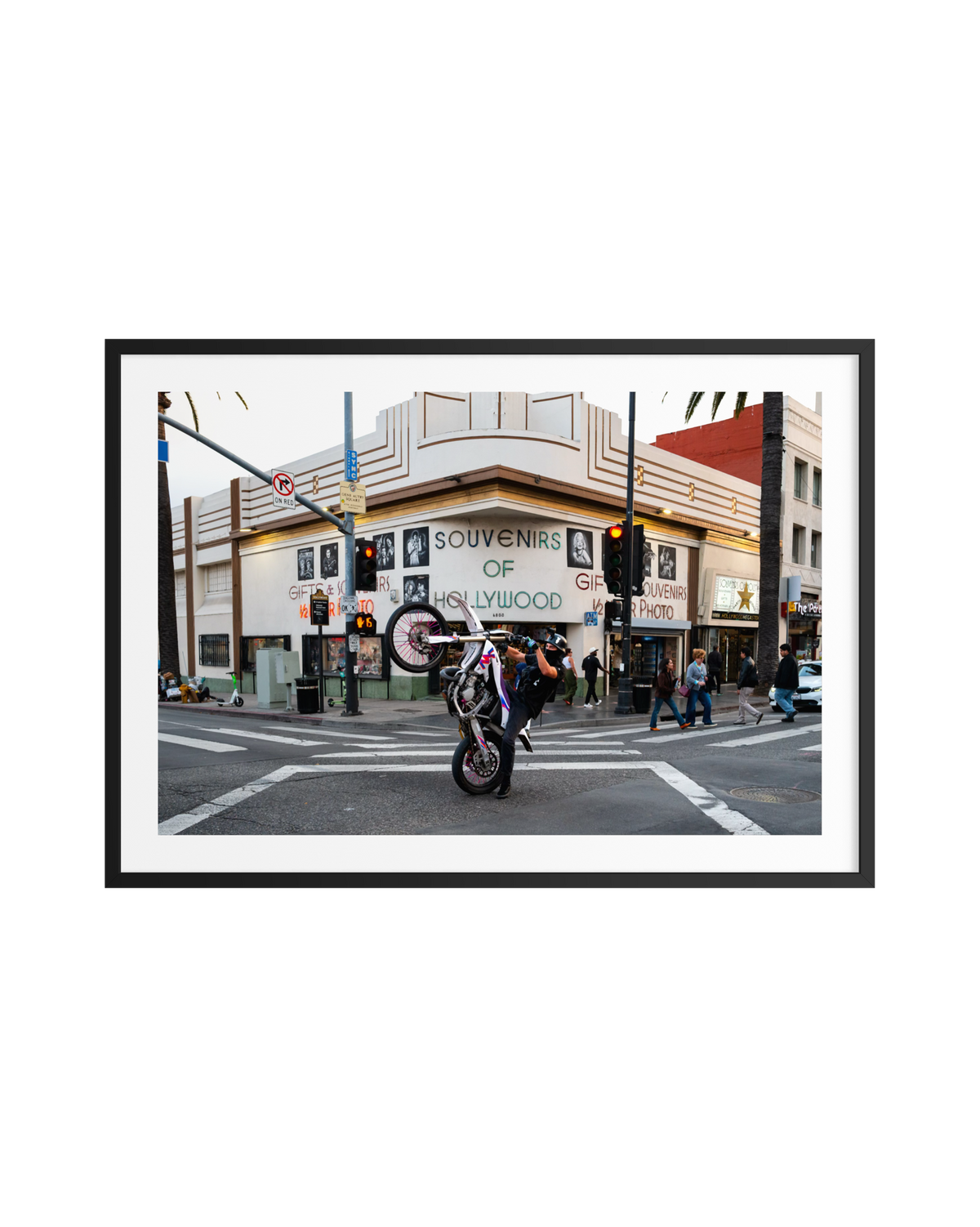 Motorcyclist performing a wheelie near the Only in Hollywood shop as tourists take photos at a busy Los Angeles intersection.