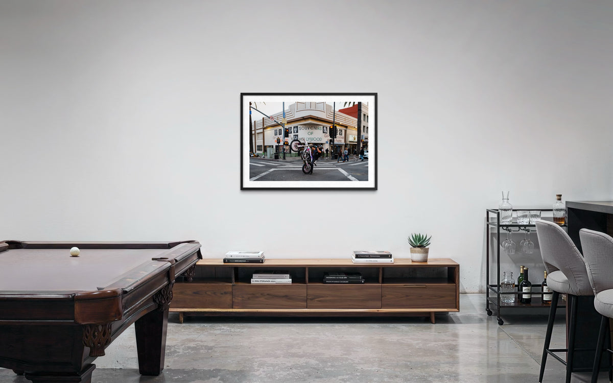 Hollywood living room with pool table, wall art, wood console, bar cart, and stools on a concrete floor.