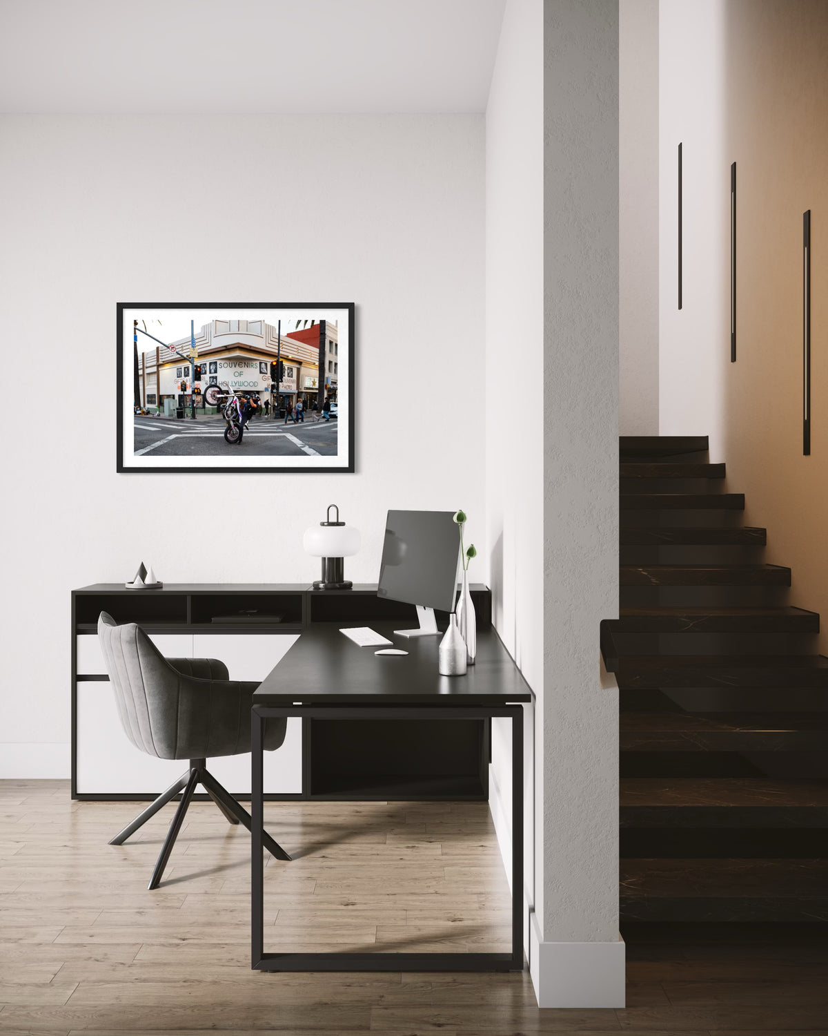 Los Angeles home office with black desk, gray chair, and “Only in Hollywood” photos by a dark staircase.