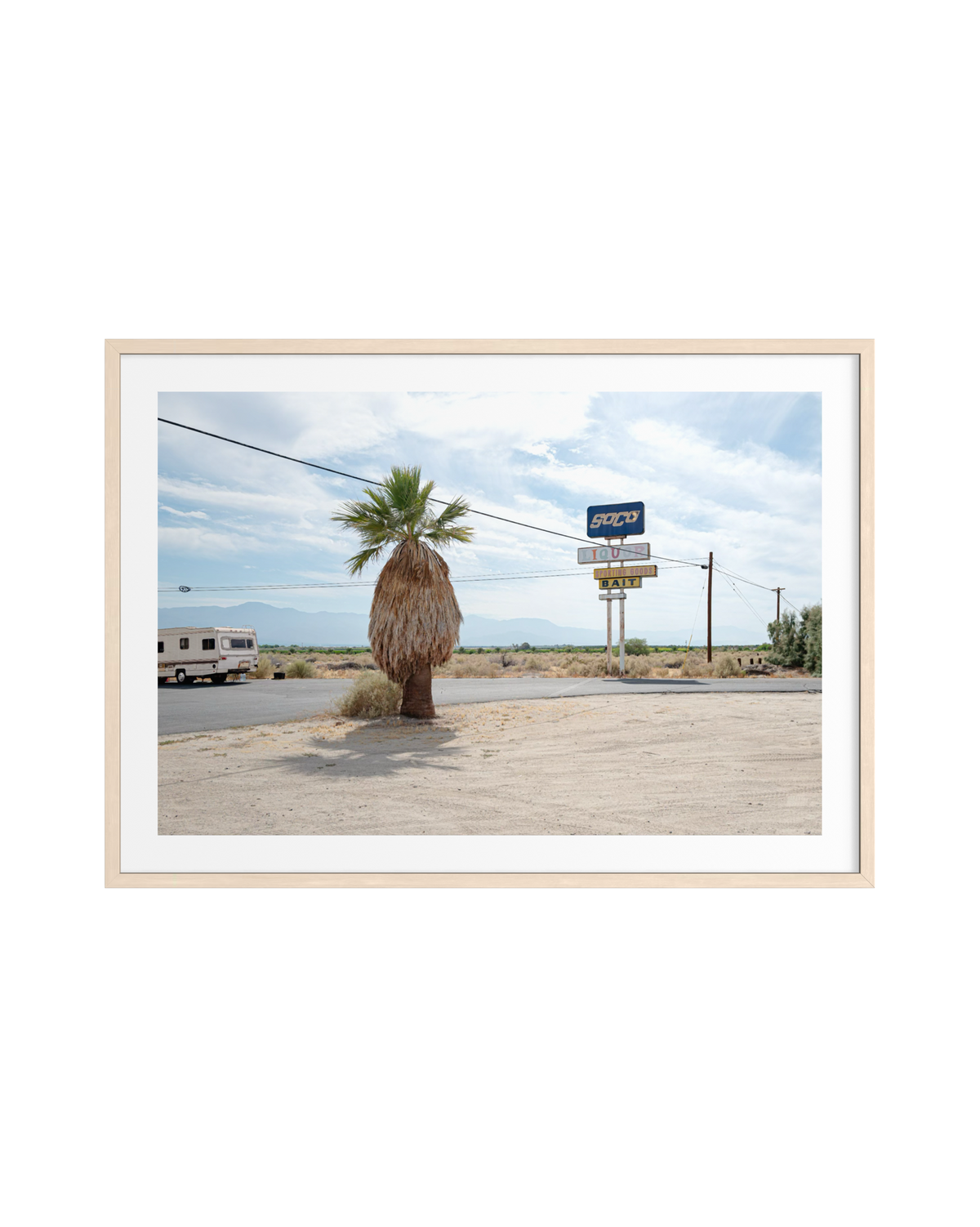 Palm tree and RV parked near a blue motel sign on a Palm Desert roadside beneath cloudy skies.