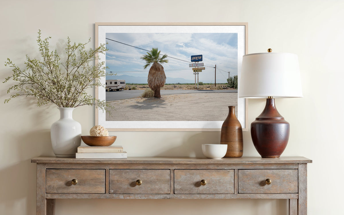 Framed photo of a palm tree and Palm Desert resort sign hangs above a rustic console table with decor.