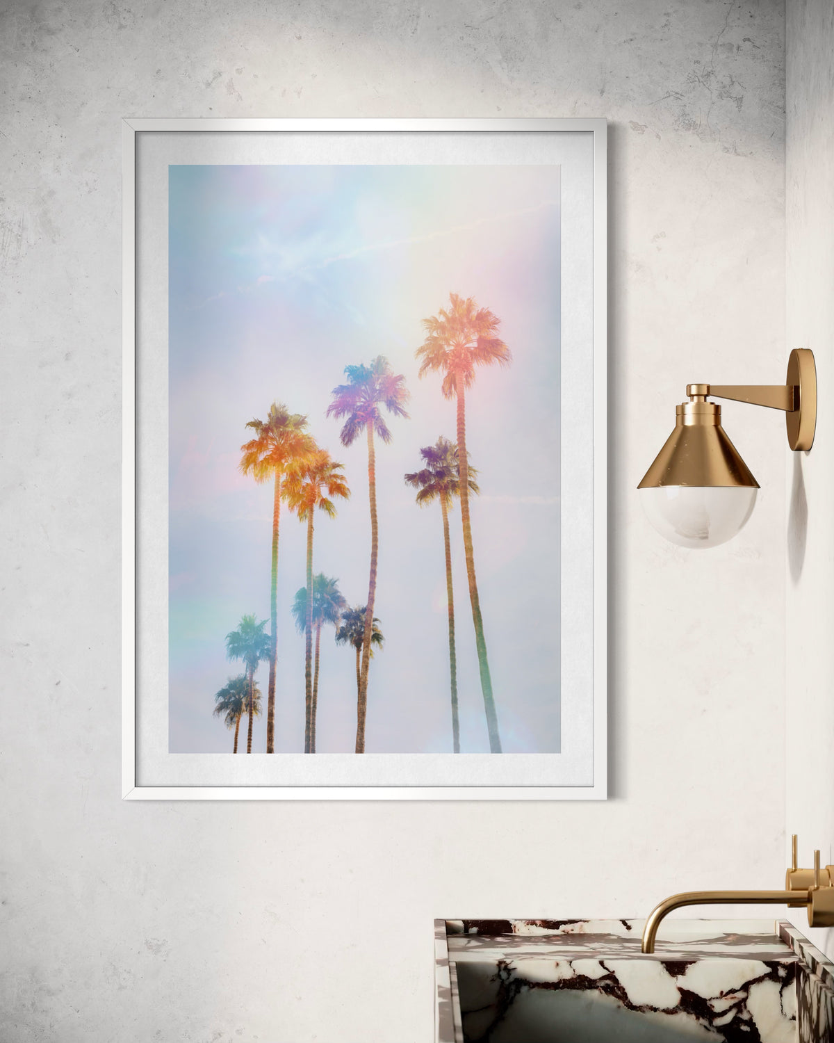 Framed photo of Palm Springs palm trees hangs above a marble sink with gold light on a white wall.