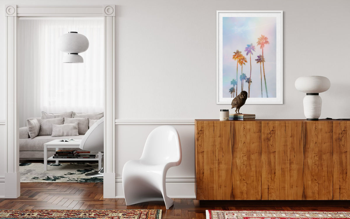Palm Springs palm trees photograph displayed on a light wall above a wooden cabinet and white chair.