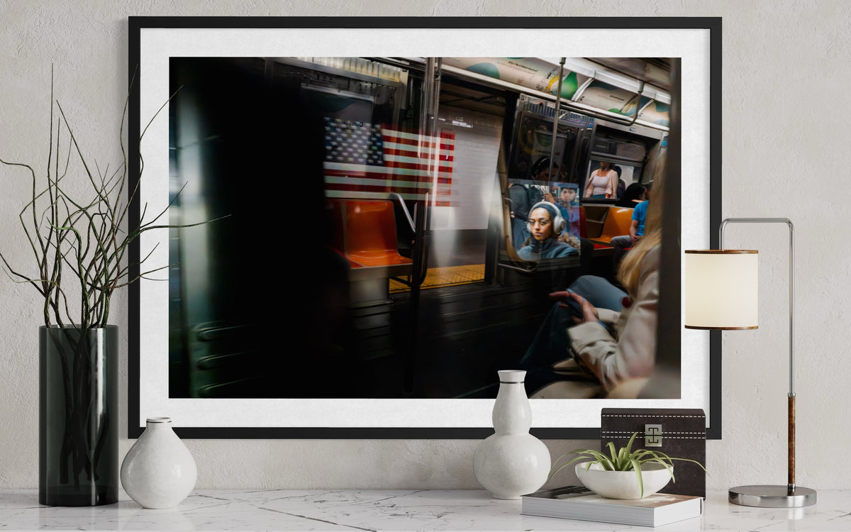 Framed photograph of a New York City subway train with a US flag and its reflection on a white marble table.