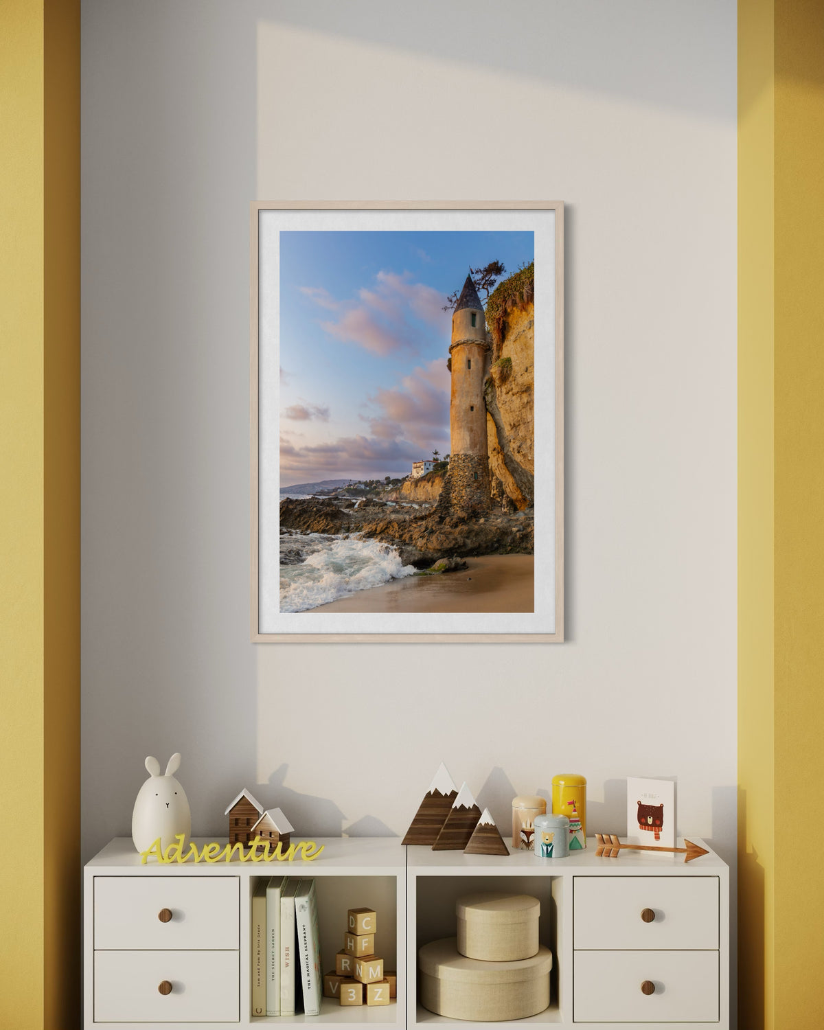 Framed photo of Laguna Beach Pirate Tower on wall above shelf with toys, books, and a yellow Adventure sign.