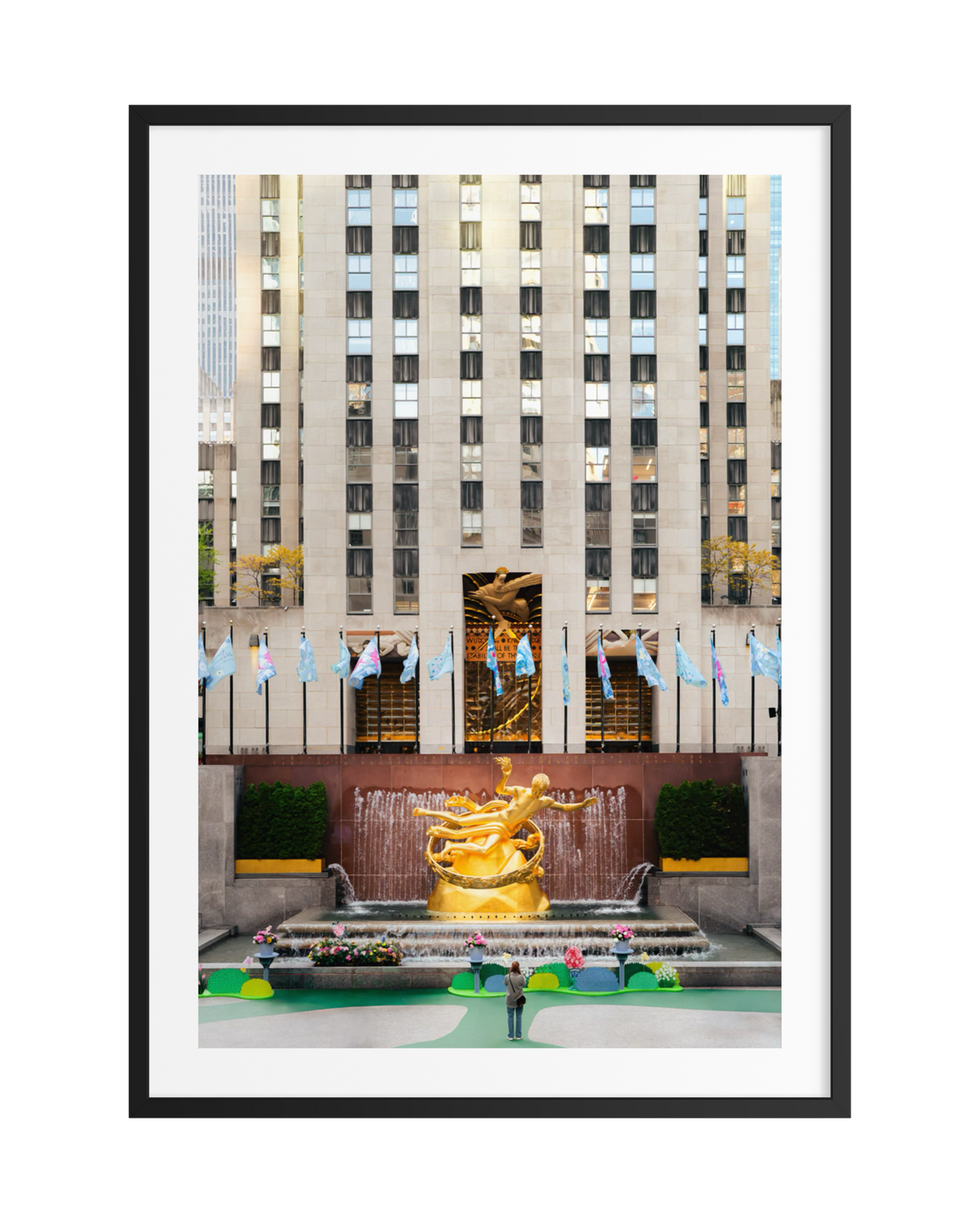 Person standing before the Prometheus statue at Rockefeller Center, NYC flags and skyscraper visible behind.