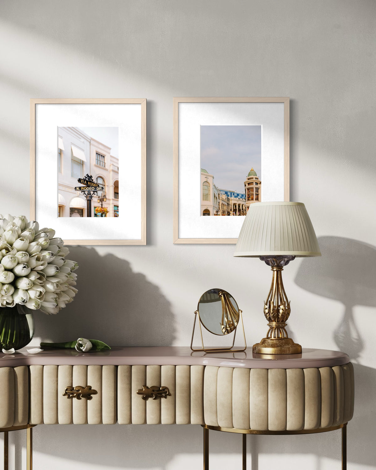 Beige console table with lamp, mirror, white flowers, and Rodeo Drive artwork against a light gray wall.