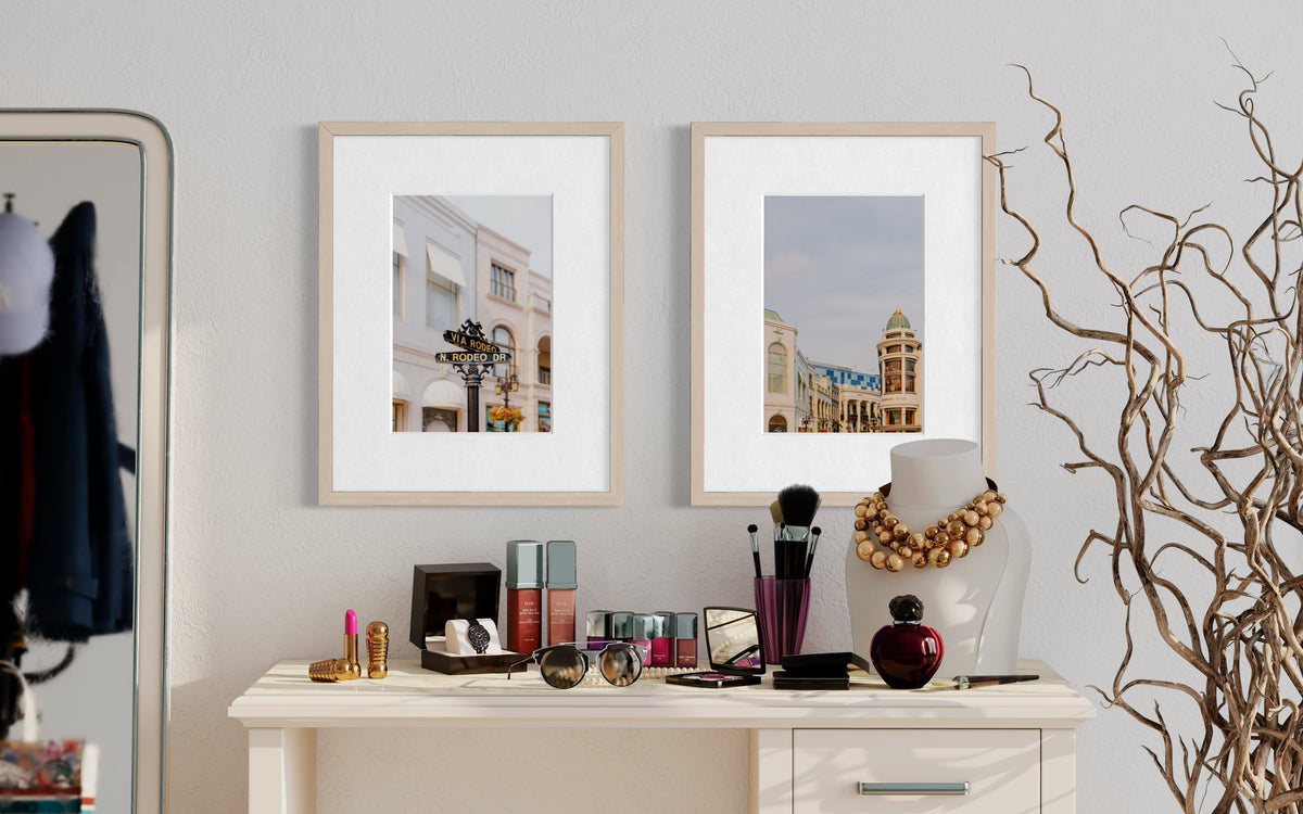 Framed prints of Beverly Hills buildings hang above a vanity with makeup and brushes.