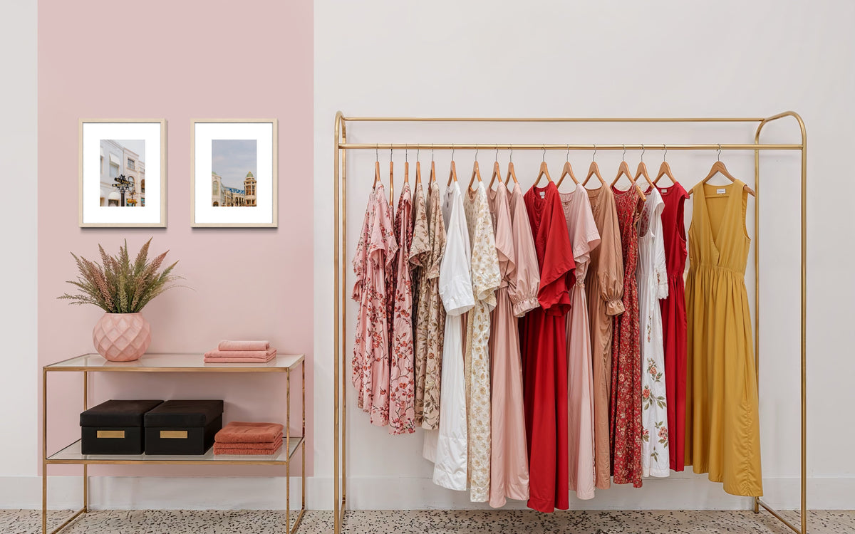 Pink, red, and yellow dresses on a rack beside a table with plant, towels, art, and Rodeo Drive photo in Beverly Hills.