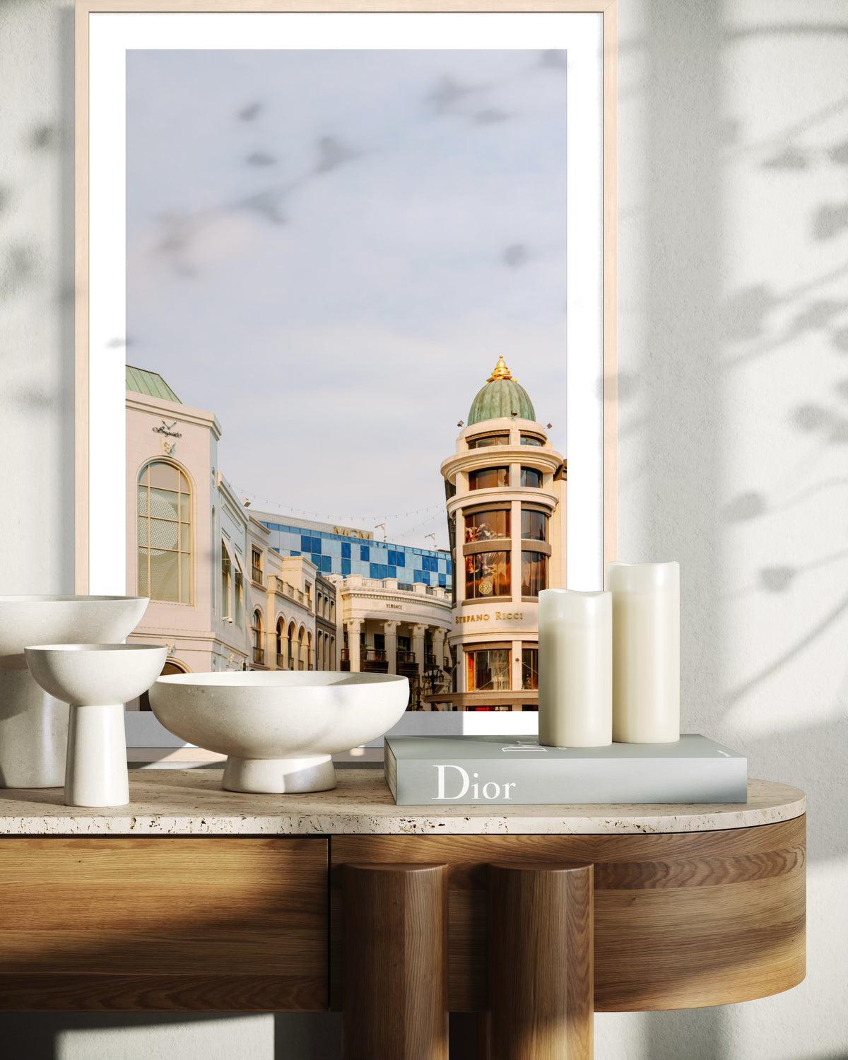 Framed Rodeo Drive print with candles, bowls, and a Dior book on a curved wood table in a Los Angeles setting.