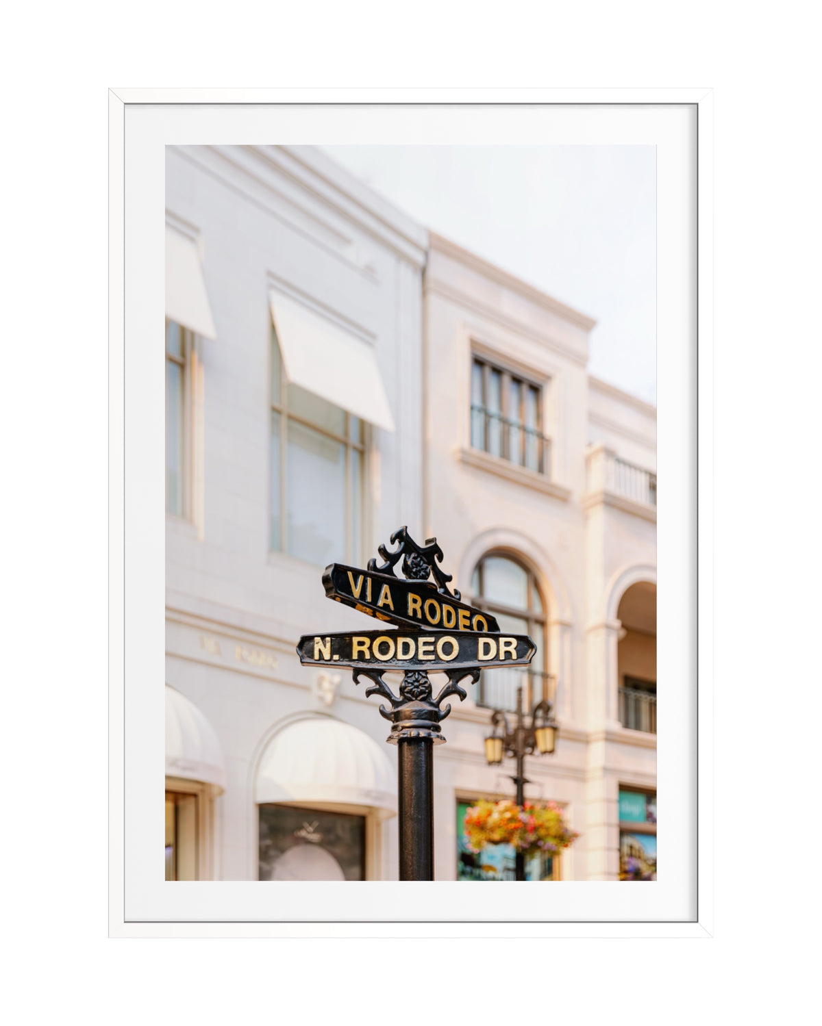 Rodeo Drive street sign in Beverly Hills, set against a white building with awnings and floral accents.