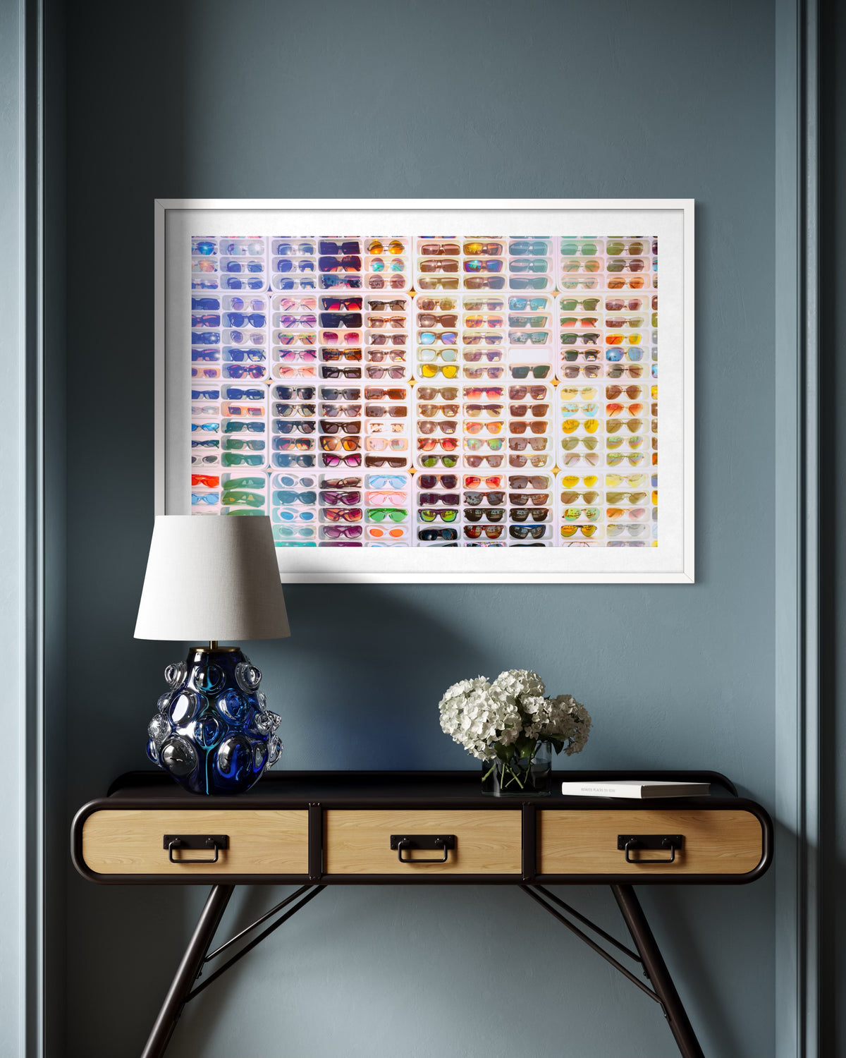Shades of Summer“ art print hangs above a console with lamp, book, and hydrangeas in a blue-walled room.