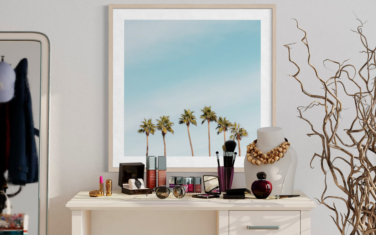 Framed photo of tall palm trees in Palm Springs beneath a clear blue sky, displayed on a dresser with makeup and jewelry.
