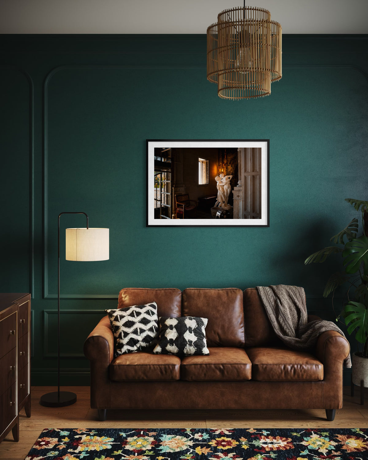 Brown leather sofa with cushions by framed art and Stolen Kiss print on a dark green wall, warm lighting.