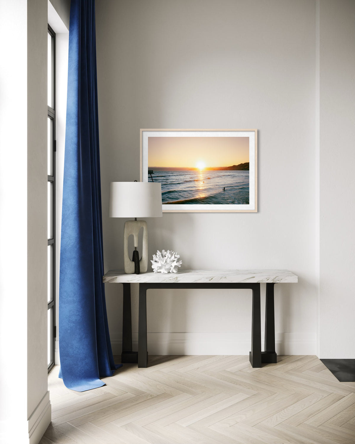 Marble console below “Surfers at Sunset” art, blue curtains in a bright entryway suggest a Pacific evening scene.
