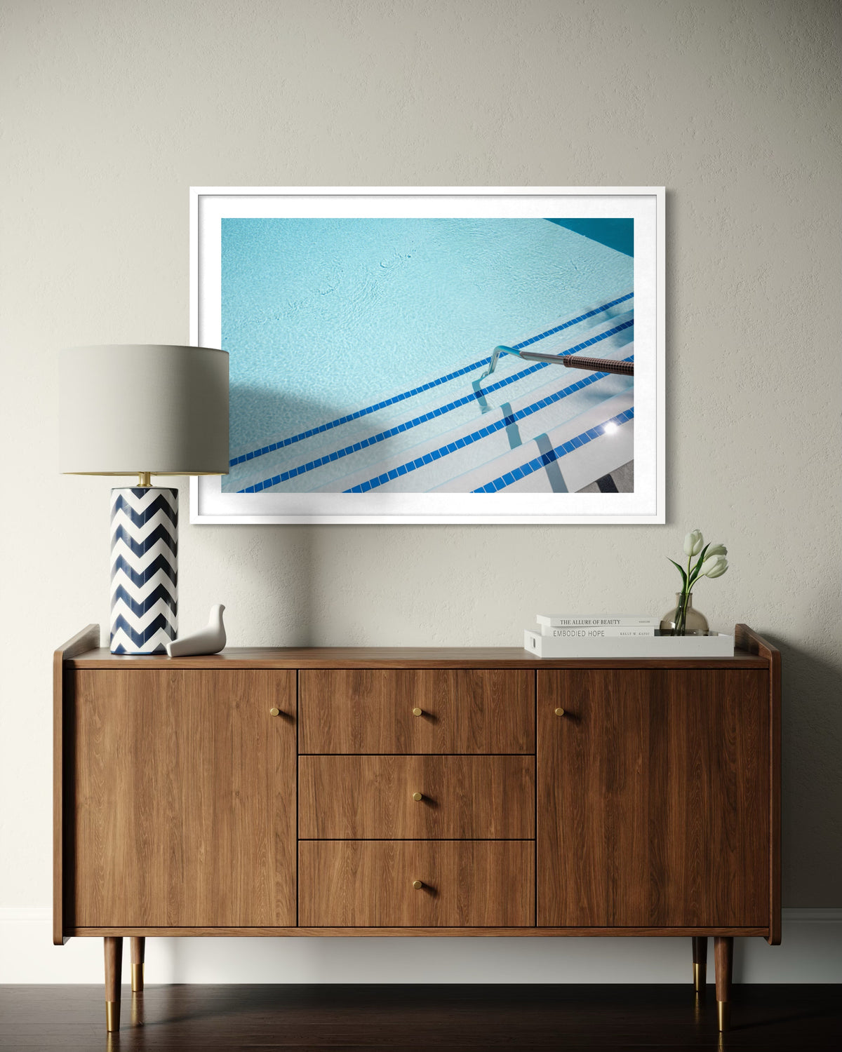 “The Hotel Pool” print hangs above a mid-century sideboard with a lamp and decor in a Palm Springs room.
