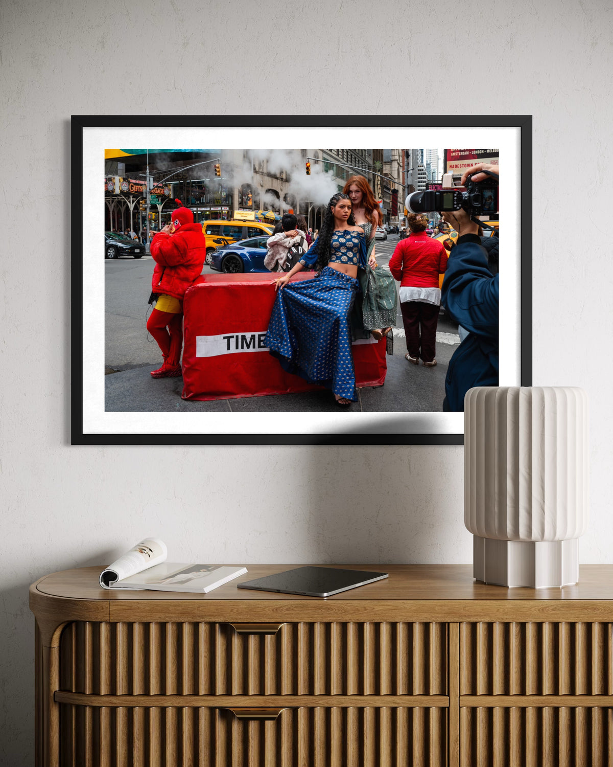 Framed street scene of Times Square Confluence displayed above a wooden sideboard with a lamp.