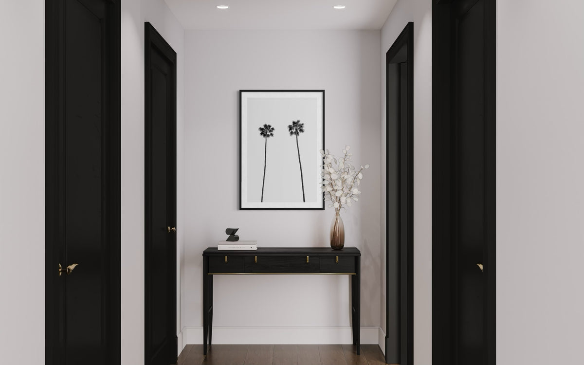 Hallway with black doors, black console, white flowers, and Twin Palms wall art; minimal decor visible.