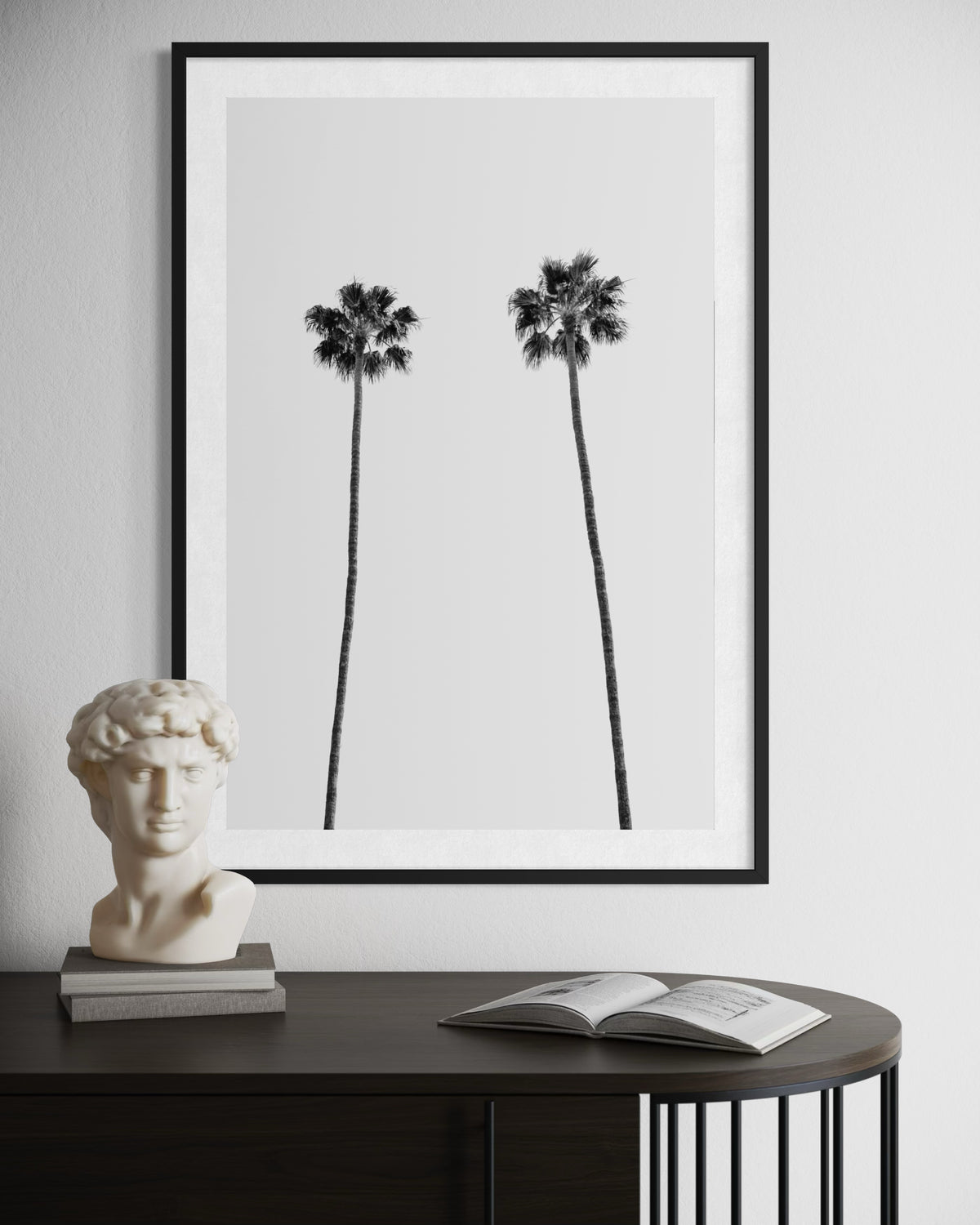 Black-and-white minimal print of two palm trees above a table with a classical bust and an open book.