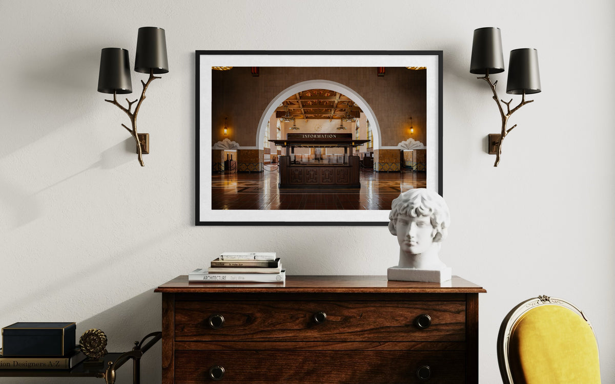 Framed Union Station Information photo above dresser with books, sculpture head, sconces, and yellow chair.