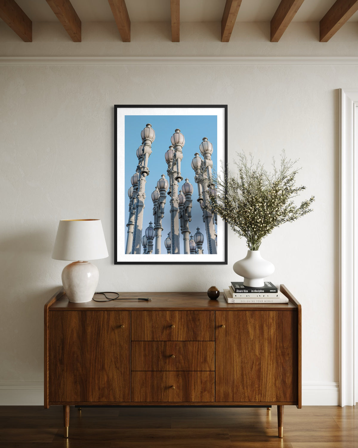 Framed photo of Los Angeles’s Urban Lights street lamps at dusk on a wooden sideboard with lamp, books, and vase.