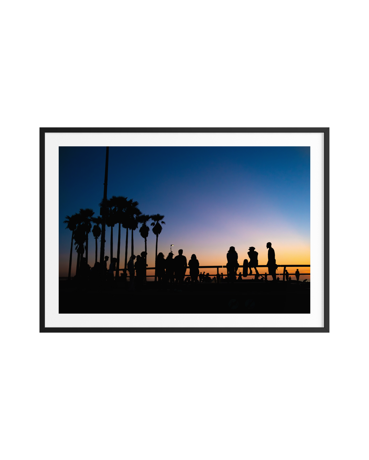 Silhouettes of people and palm trees at sunset on Venice Beach under a vibrant, colorful sky.