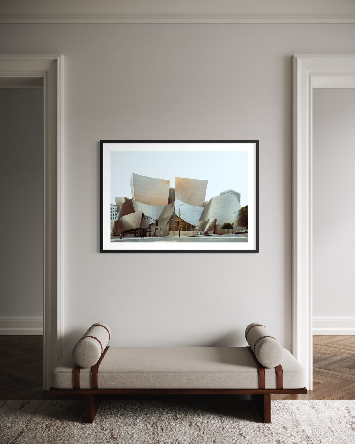 Walt Disney Concert Hall in Los Angeles, pictured in a black frame on a neutral wall above a beige bench.