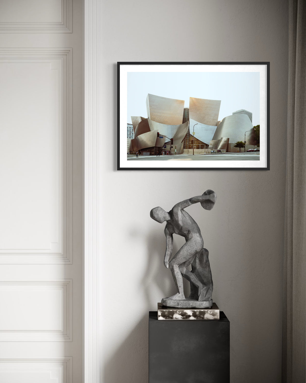 Framed photograph of Walt Disney Concert Hall in Los Angeles above a dark pedestal with an abstract sculpture.