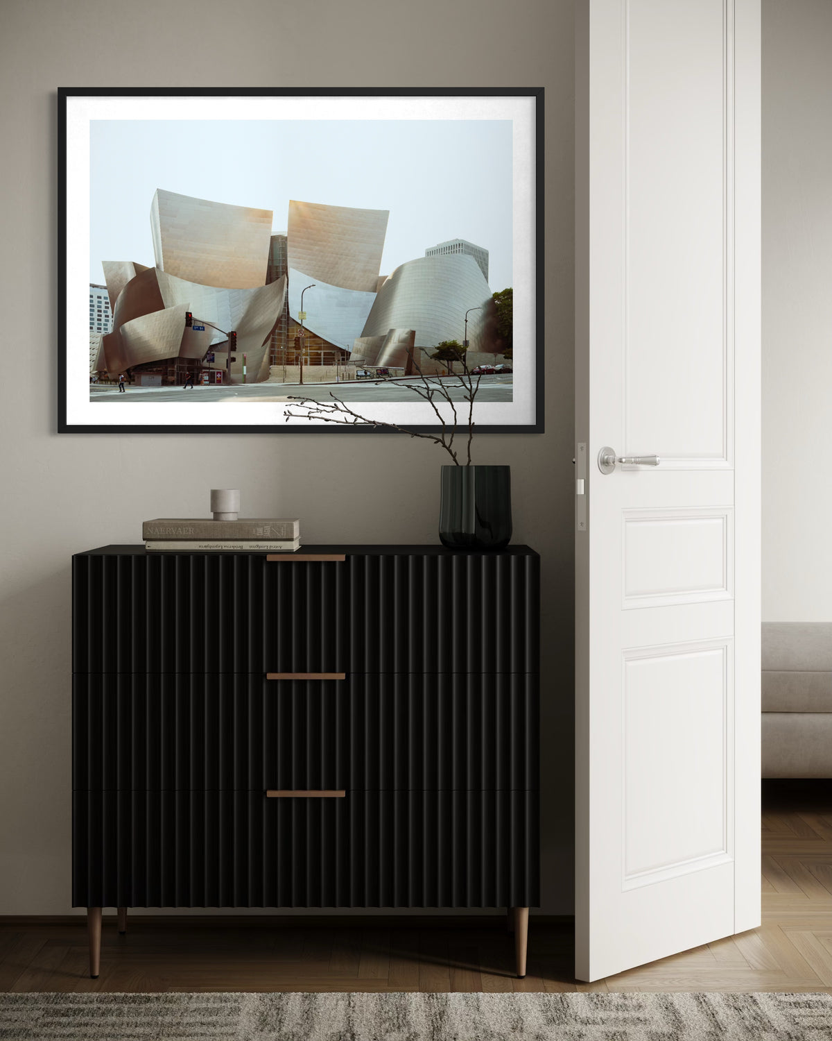 Framed photograph of Walt Disney Concert Hall in Los Angeles above a black dresser with books and a vase.