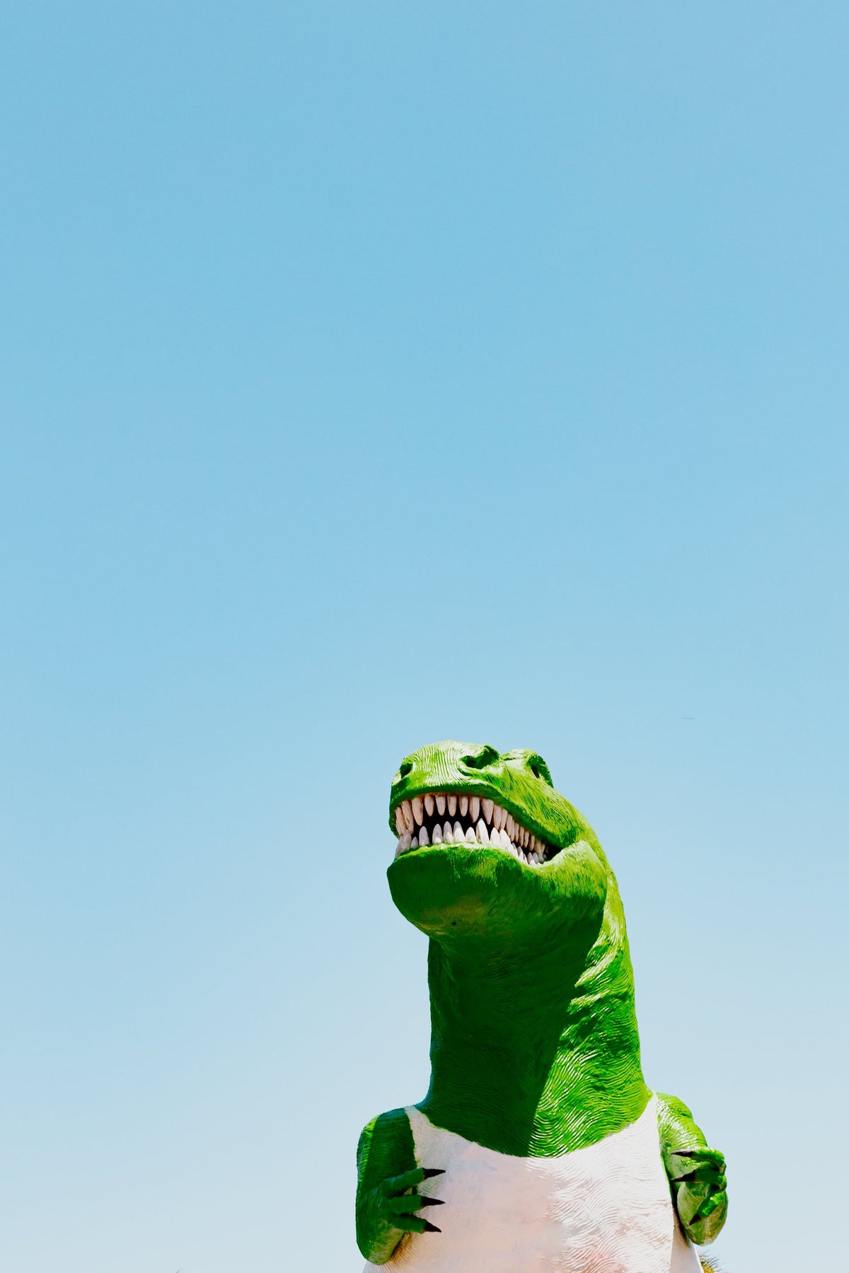 Large dinosaur statue with sharp teeth stands outdoors under a clear sky in California.