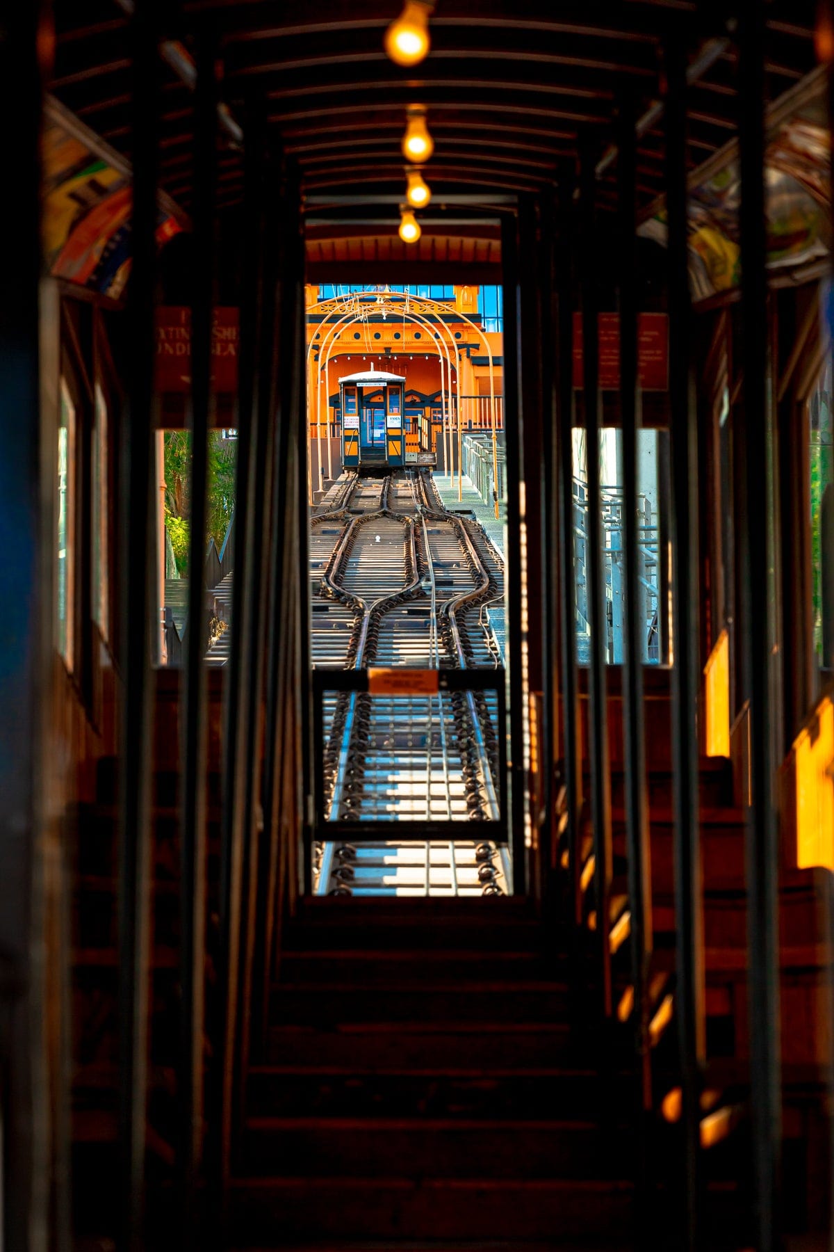 Inside a DTLA funicular car, looking up the tracks at a bright orange station in downtown Los Angeles.