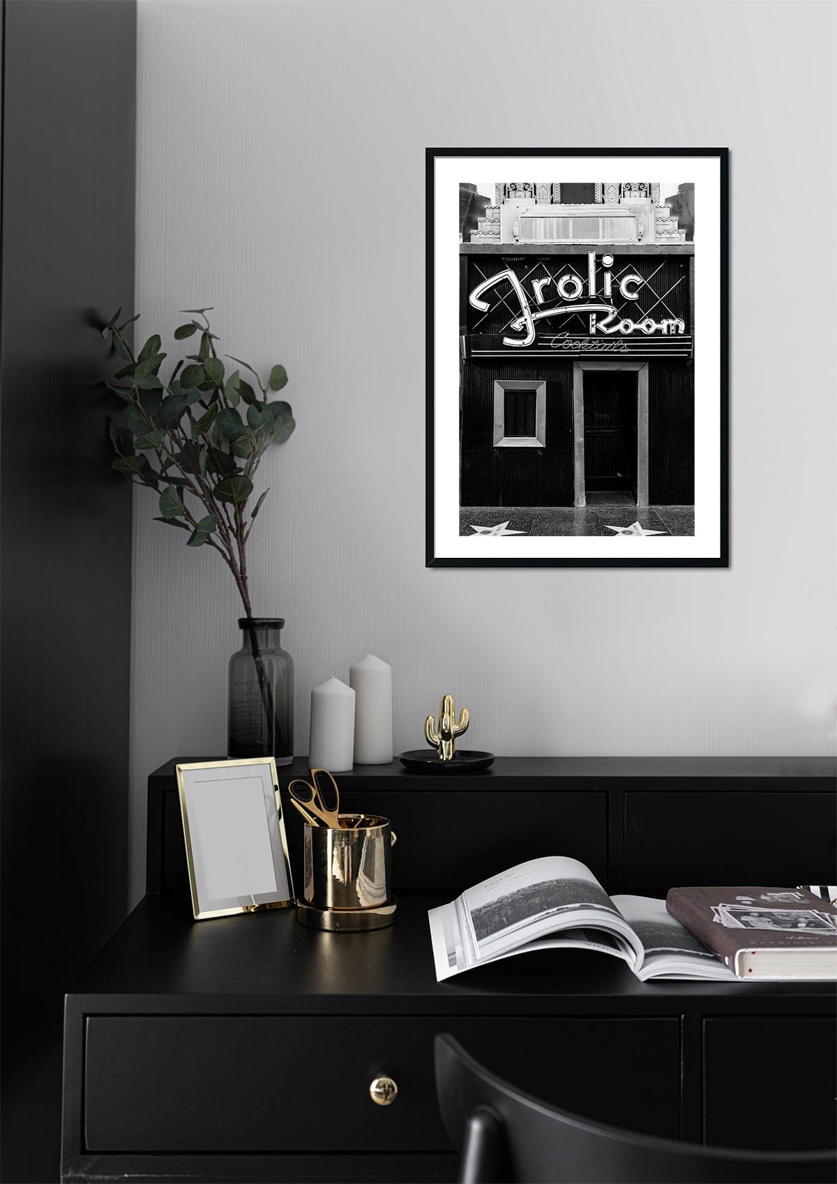 Framed Frolic Room photograph displayed above a black desk with decor, set against a pale wall in Hollywood.