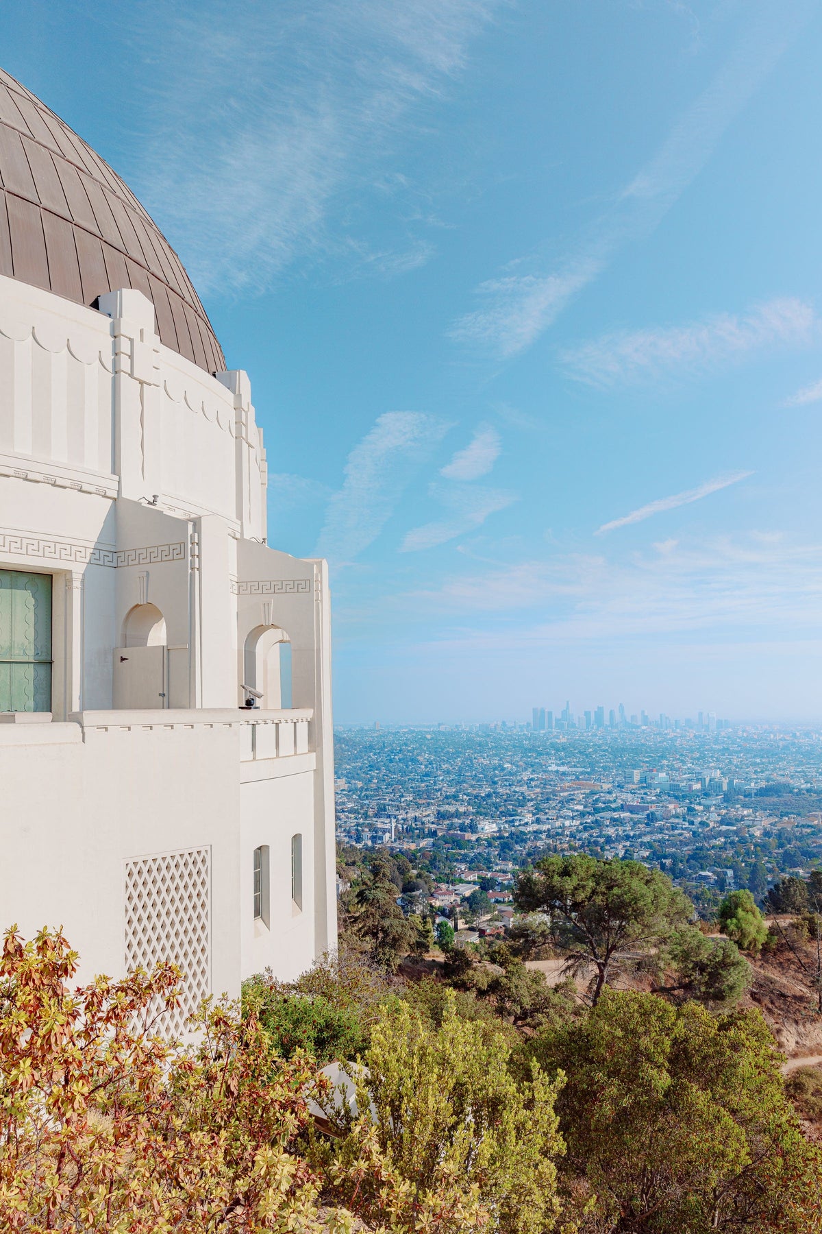 Los Angeles cityscape seen from Griffith Observatory under a clear sky, with skyline buildings in the distance.