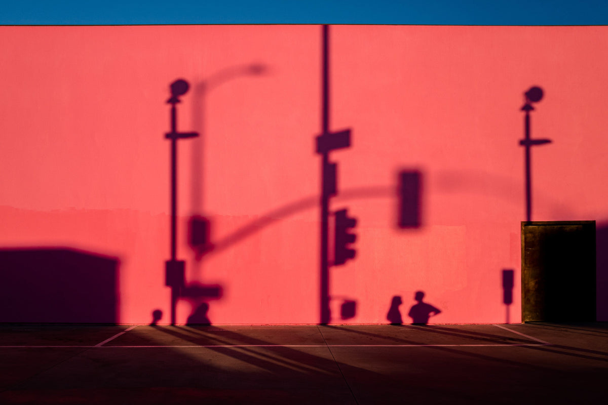 The pink facade of That Pink Wall in Los Angeles, with shadows, streetlights, and a door on the right under blue sky.