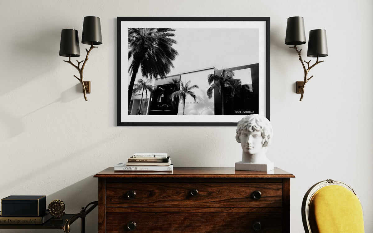Framed Beverly Hills street scene hangs above a wooden dresser, white bust, and black wall sconces.