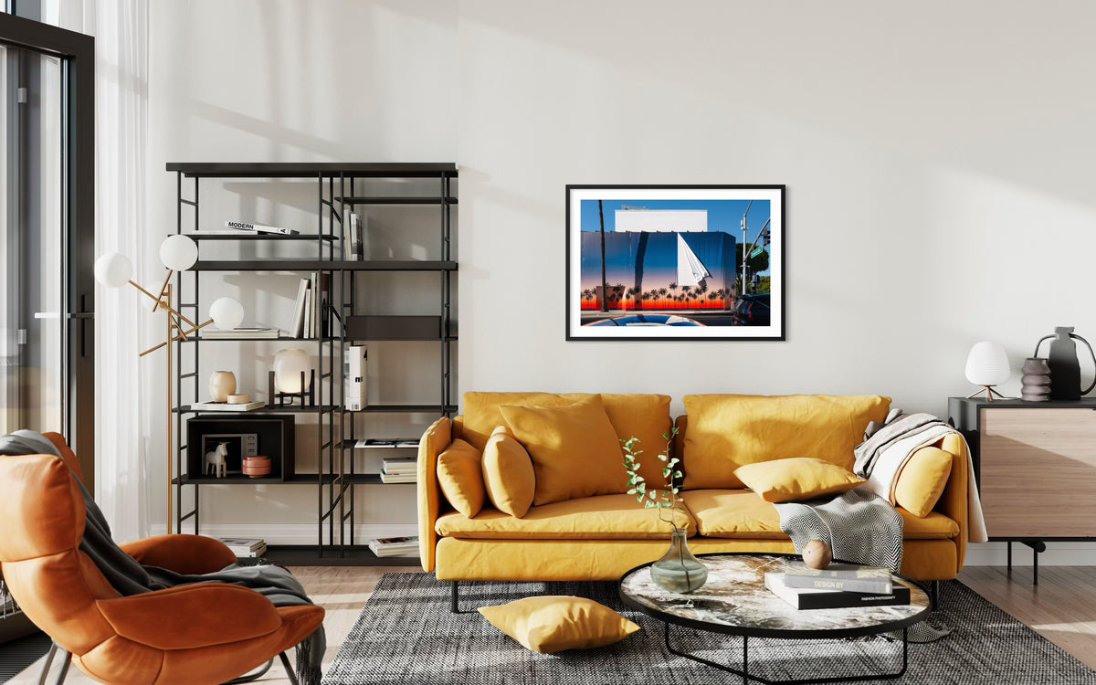 Yellow sofa and black shelves in a Beverly Hills living room, sailboat photo above glass coffee table.