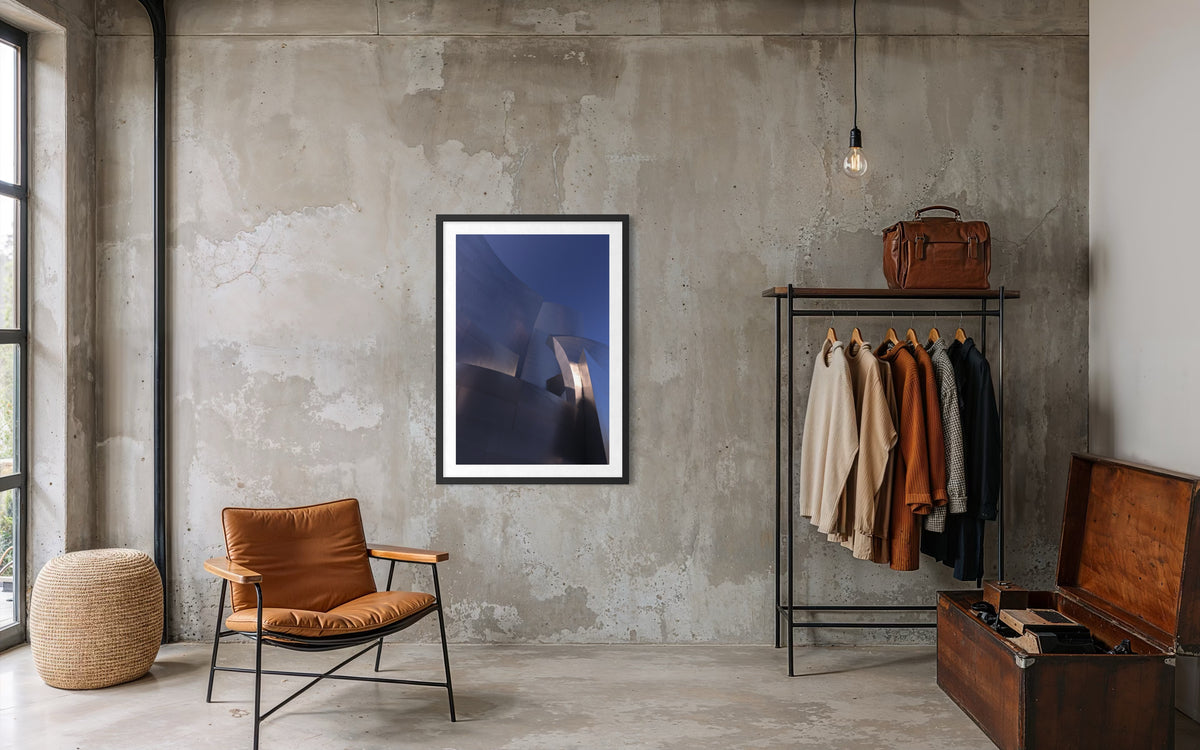 Blue Gehry leather chair, abstract painting, and suitcase in a modern room with concrete walls.