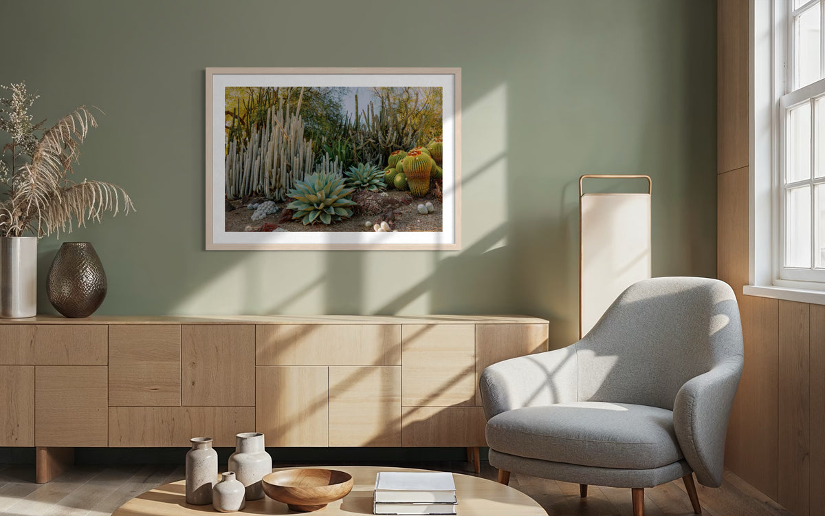 Gray chair and wood table in sunlit living room with “Cactus Garden I” art on a green wall.