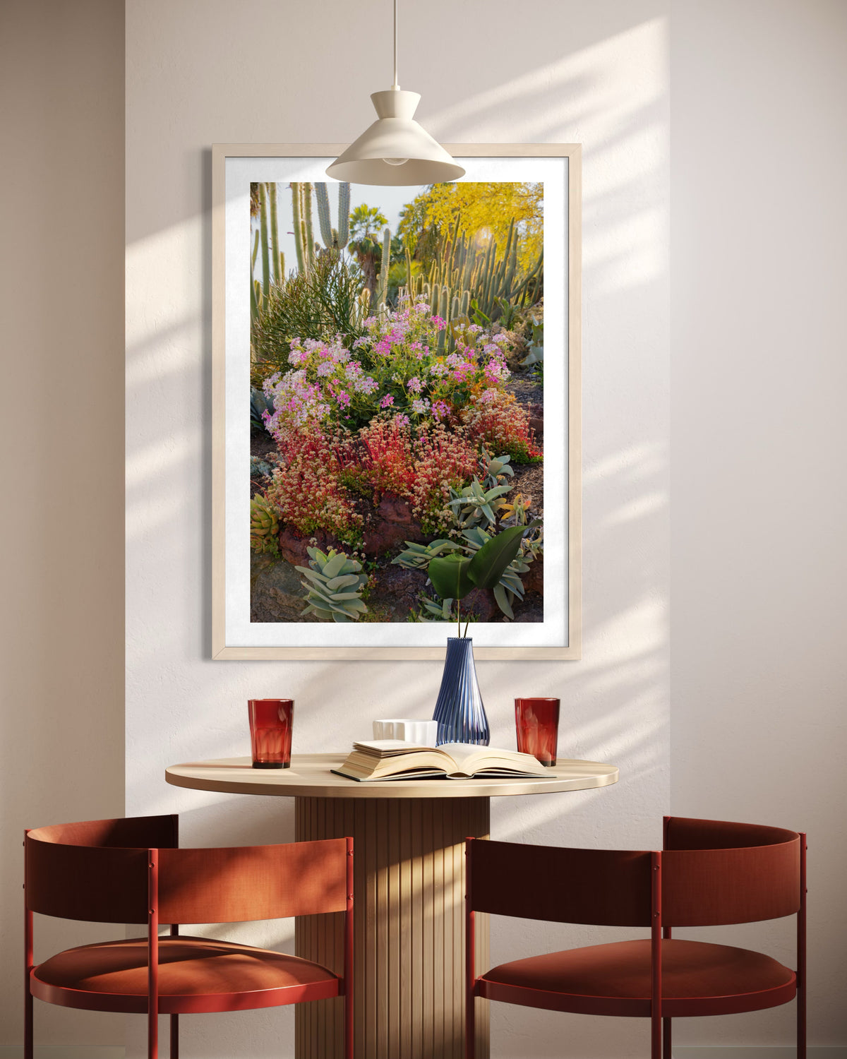Two red chairs and small table with glasses, book, and desert plant below Cactus Garden II art and pendant lamp.