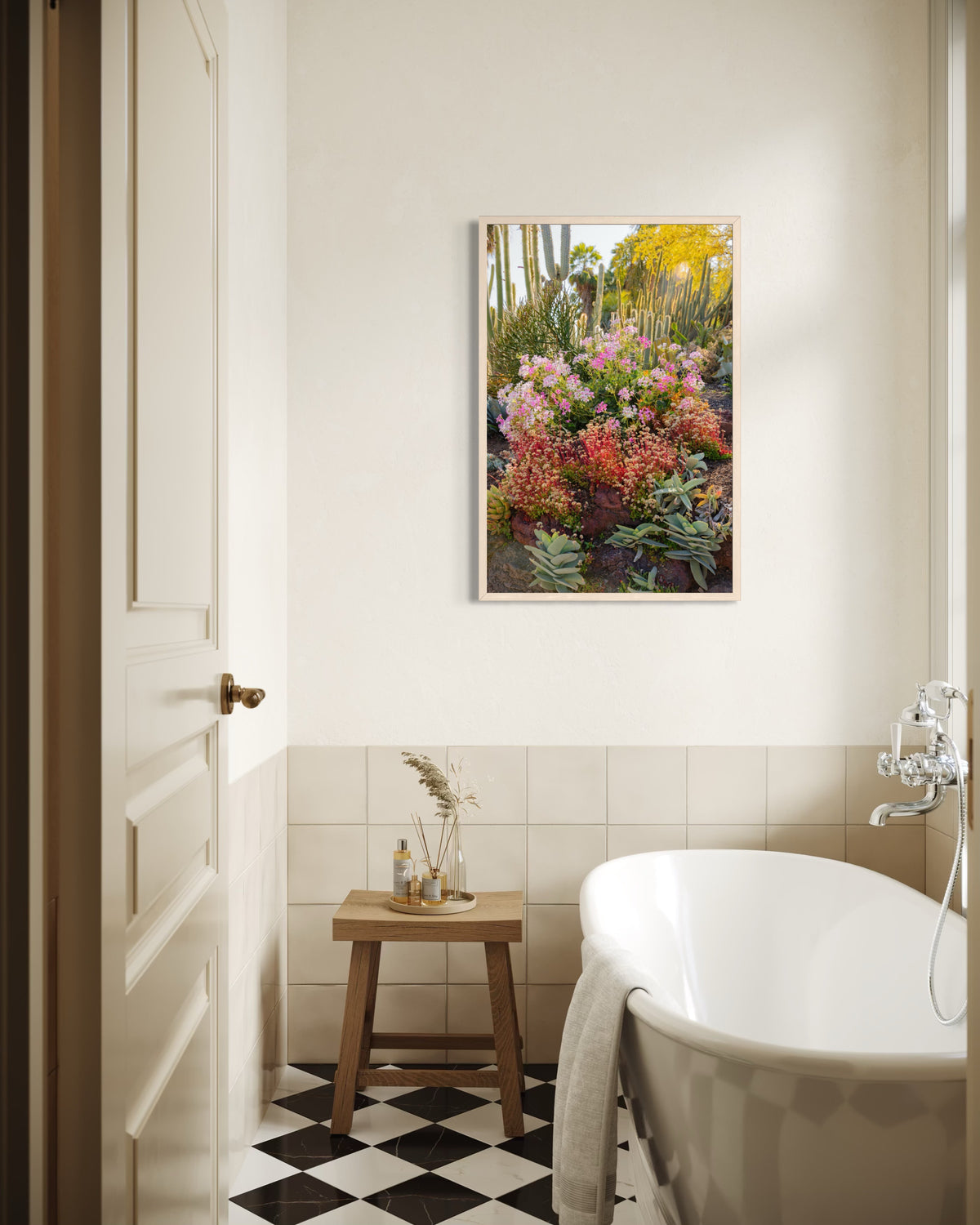 White bathtub with wood stool, beige tiles, green plants, and Cactus Garden II artwork above the tub in bright bathroom.