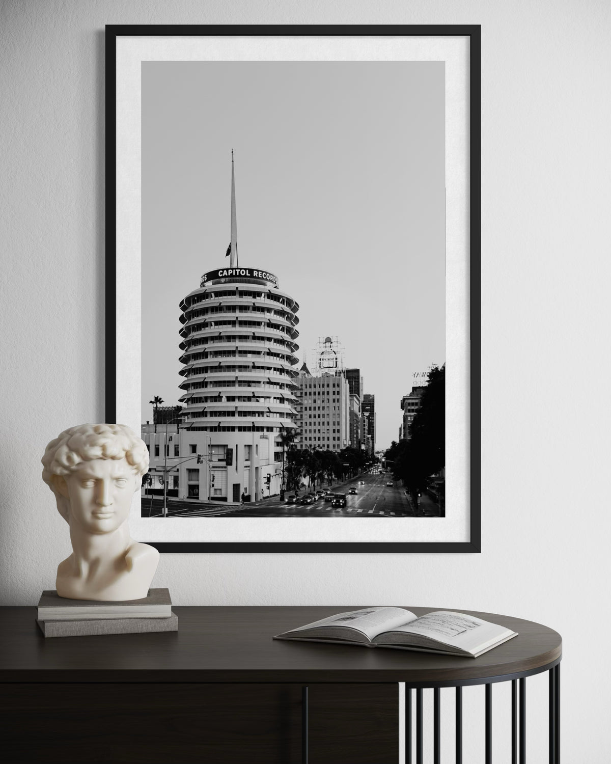Black-and-white Capitol Records Building photo, Los Angeles, displayed above table with David bust and open book.